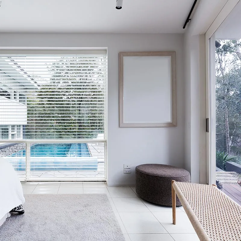 Bright bedroom with venetian blinds over a window looking onto a pool