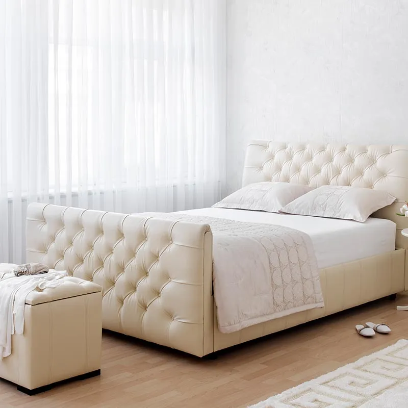 Bedroom with sheer white curtains behind a tufted cream bed