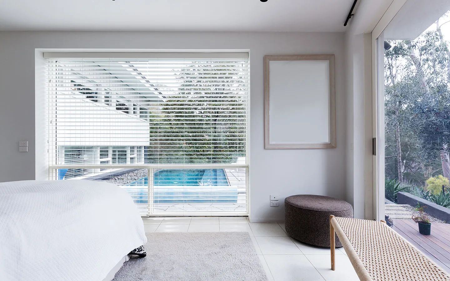 Bedroom with white venetian blinds over a large window looking onto a pool