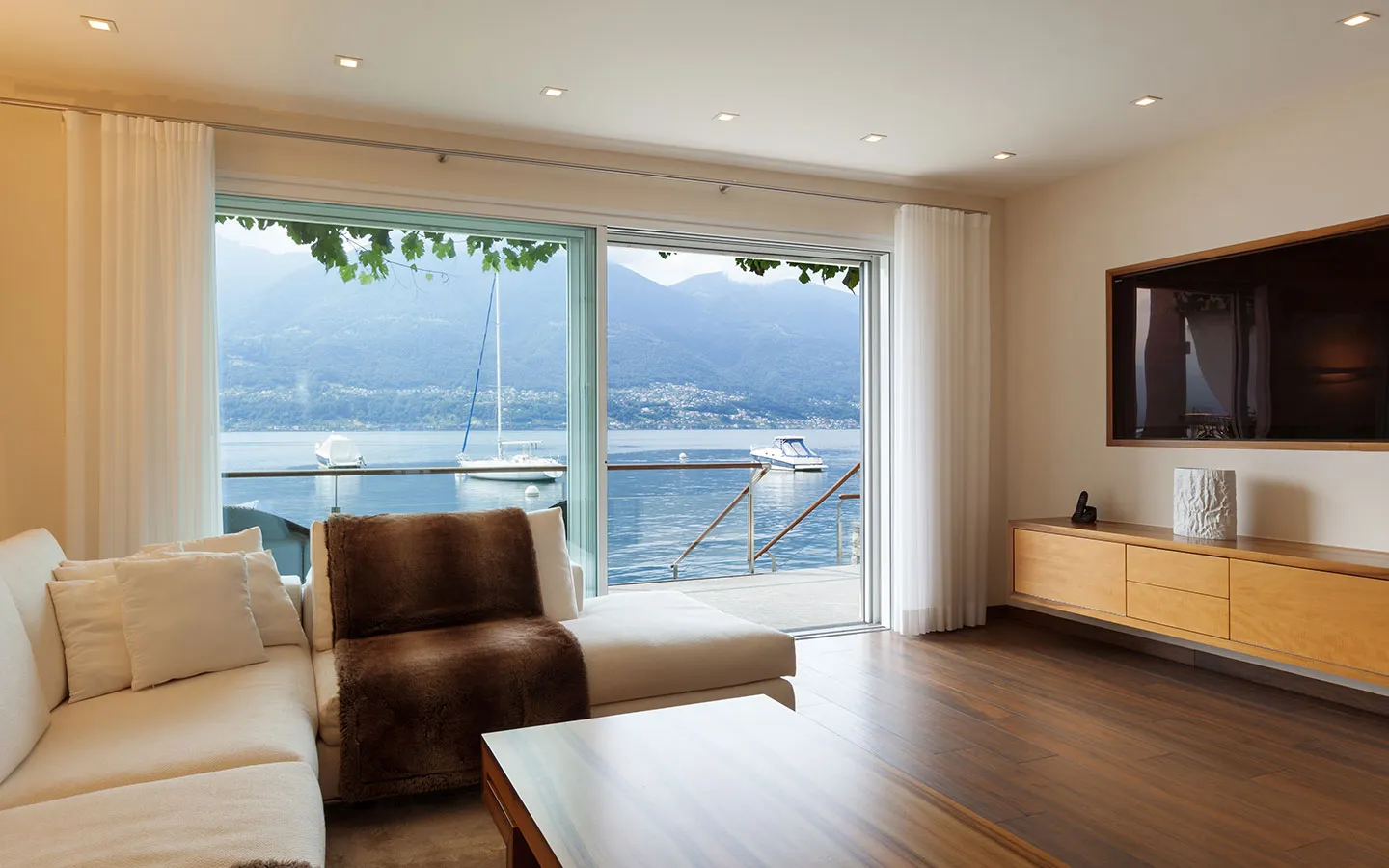 Living room with white sheer curtains across a sliding door onto a lake view