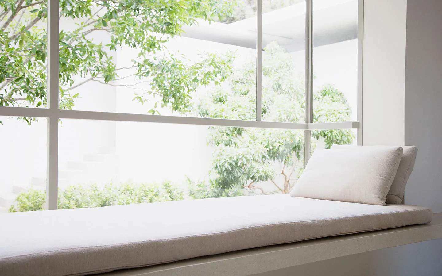 Window seat with a cream cushion and two pillows overlooking trees