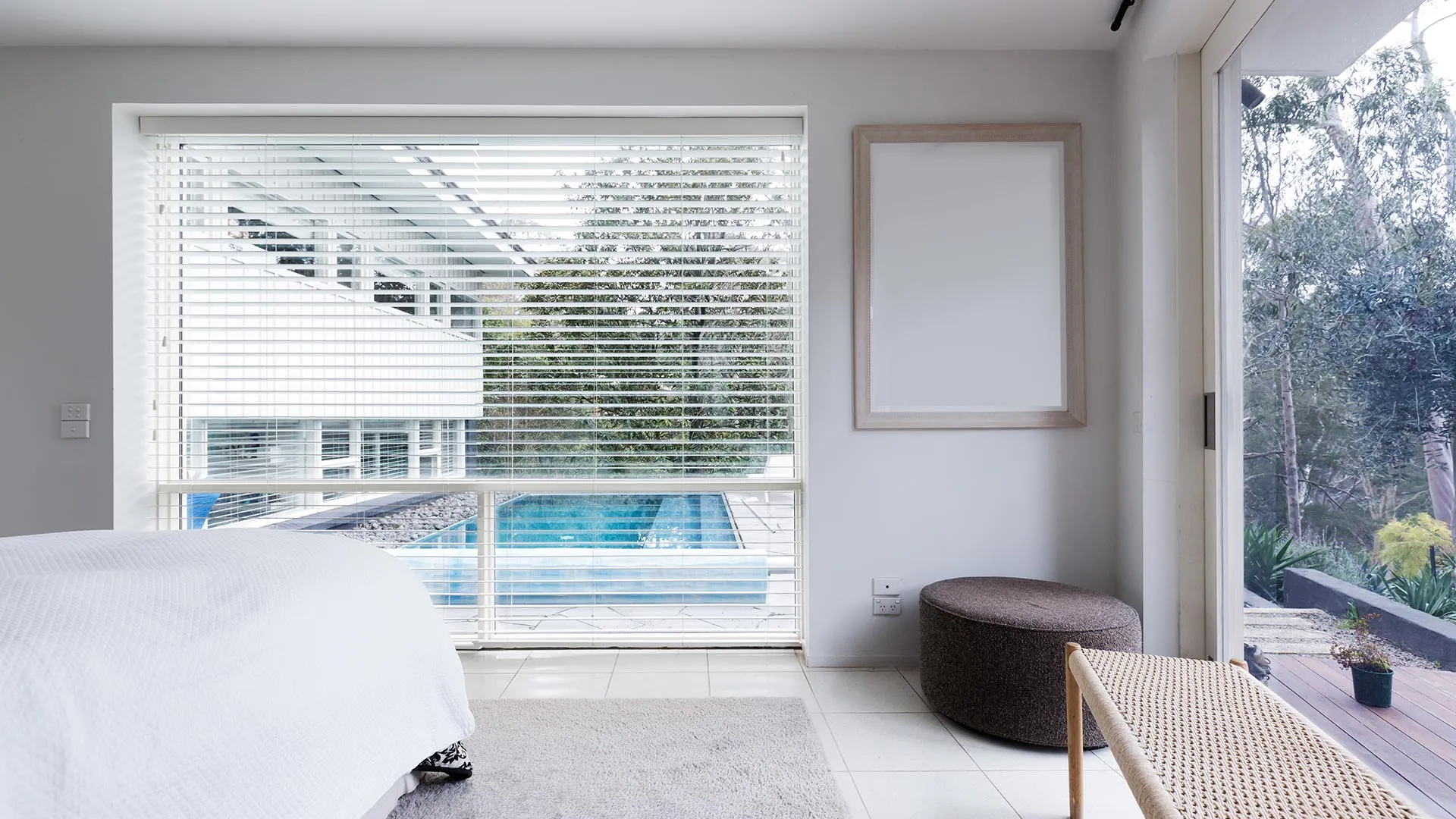 Bedroom with white venetian blinds overlooking a pool