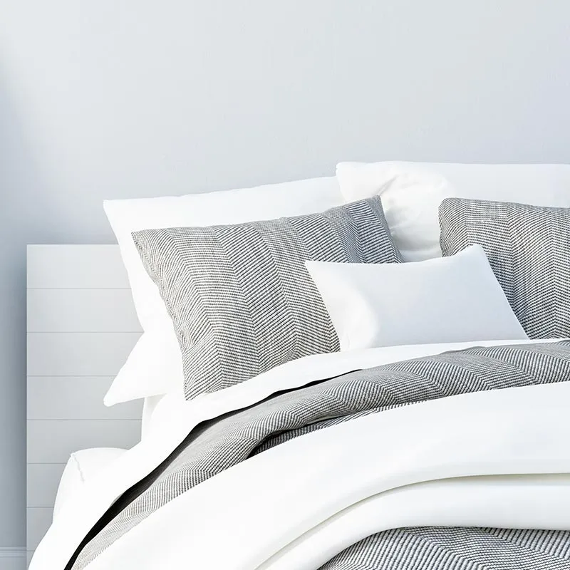 White bed dressed with grey patterned cushions and a throw